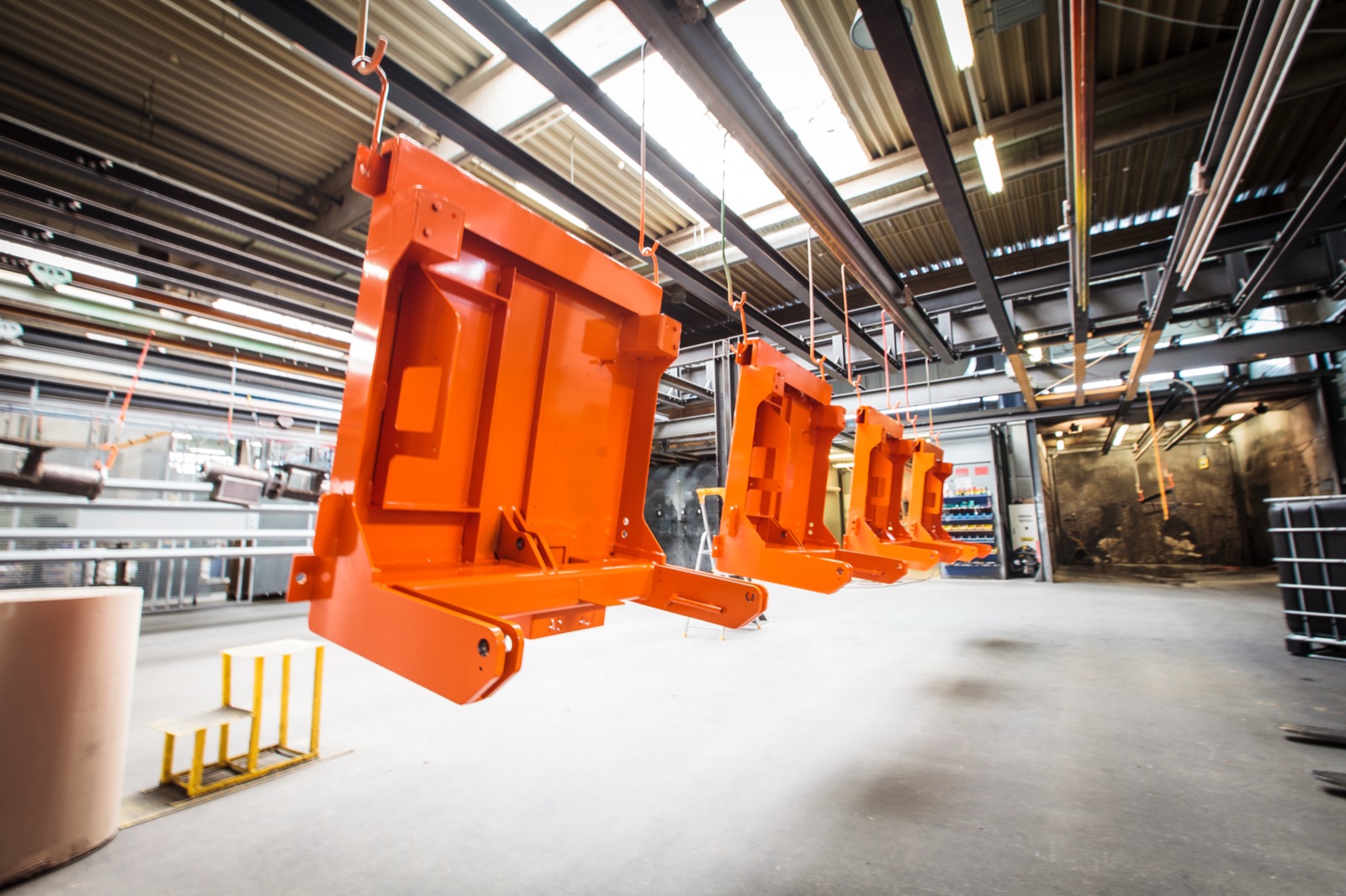 Orange beschichtete Bauteile hängen in einer Werkhalle